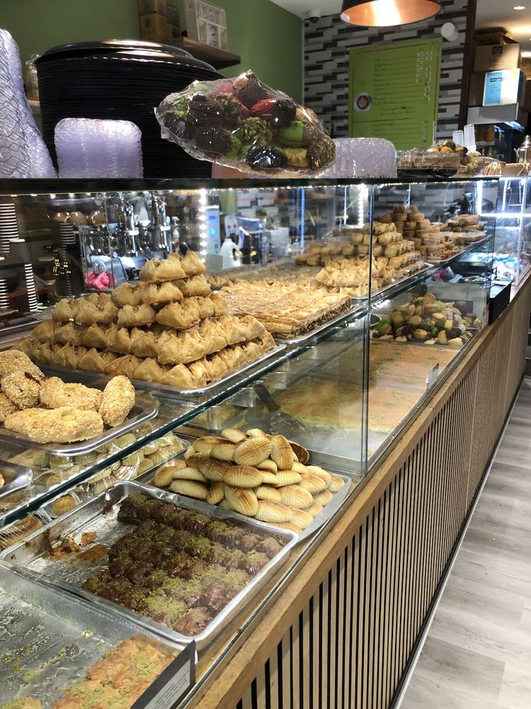 The curved glass display cabinet inside the cafe, filled with rows of pastries, seen down its length into the green-walled room.